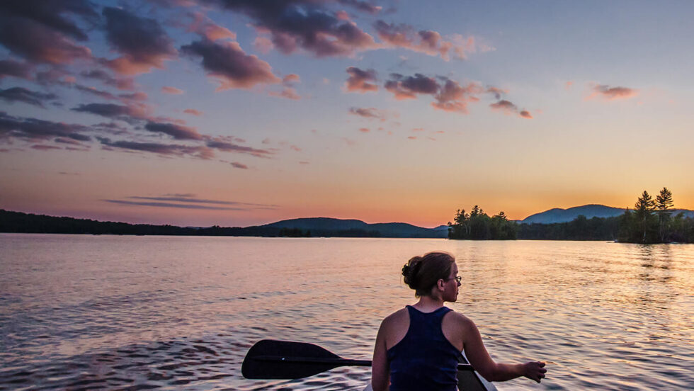Woman paddling a canoe at sunset at Paul Smith's College