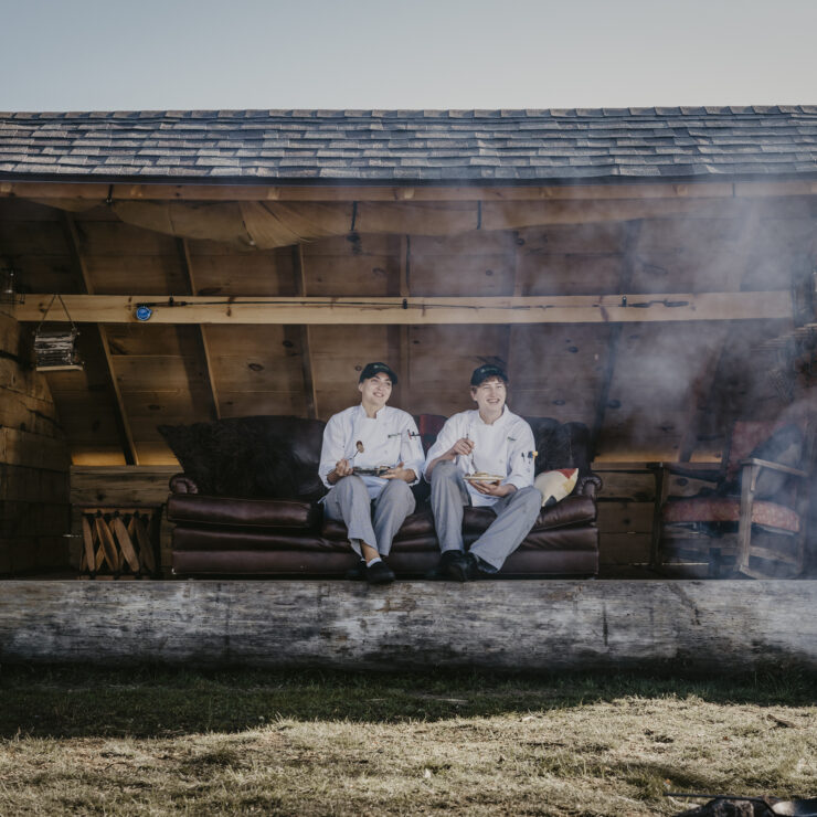 Two people sitting in a lean to with plates of food