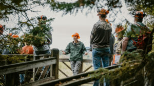 Forestry professor in raincoat on a deck next to a lake, talking to a group of students, in raincoats and hard hats