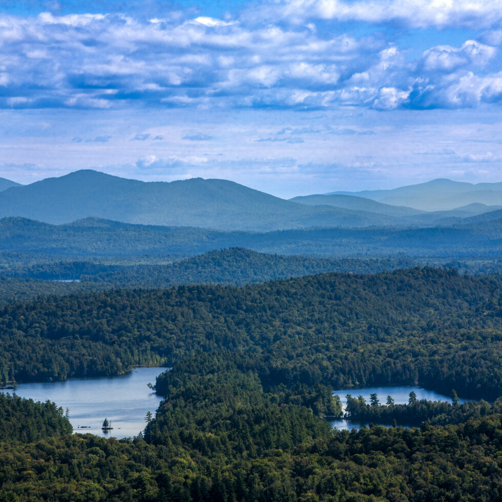 Landscape with mountains, lakes, and forests with puffy clouds in the sky