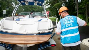 A man in a blue vest and orange hard hat sprays a motorboat with water
