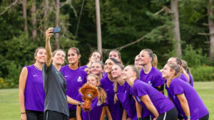 A group of people in purple shirts looking up at a cell phone
