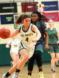 A basketball player in a white jersey dribbles around another player in a grey and green jersey.