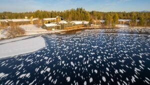 Aerial view of a frozen lake with snow drifts and a building on the shore